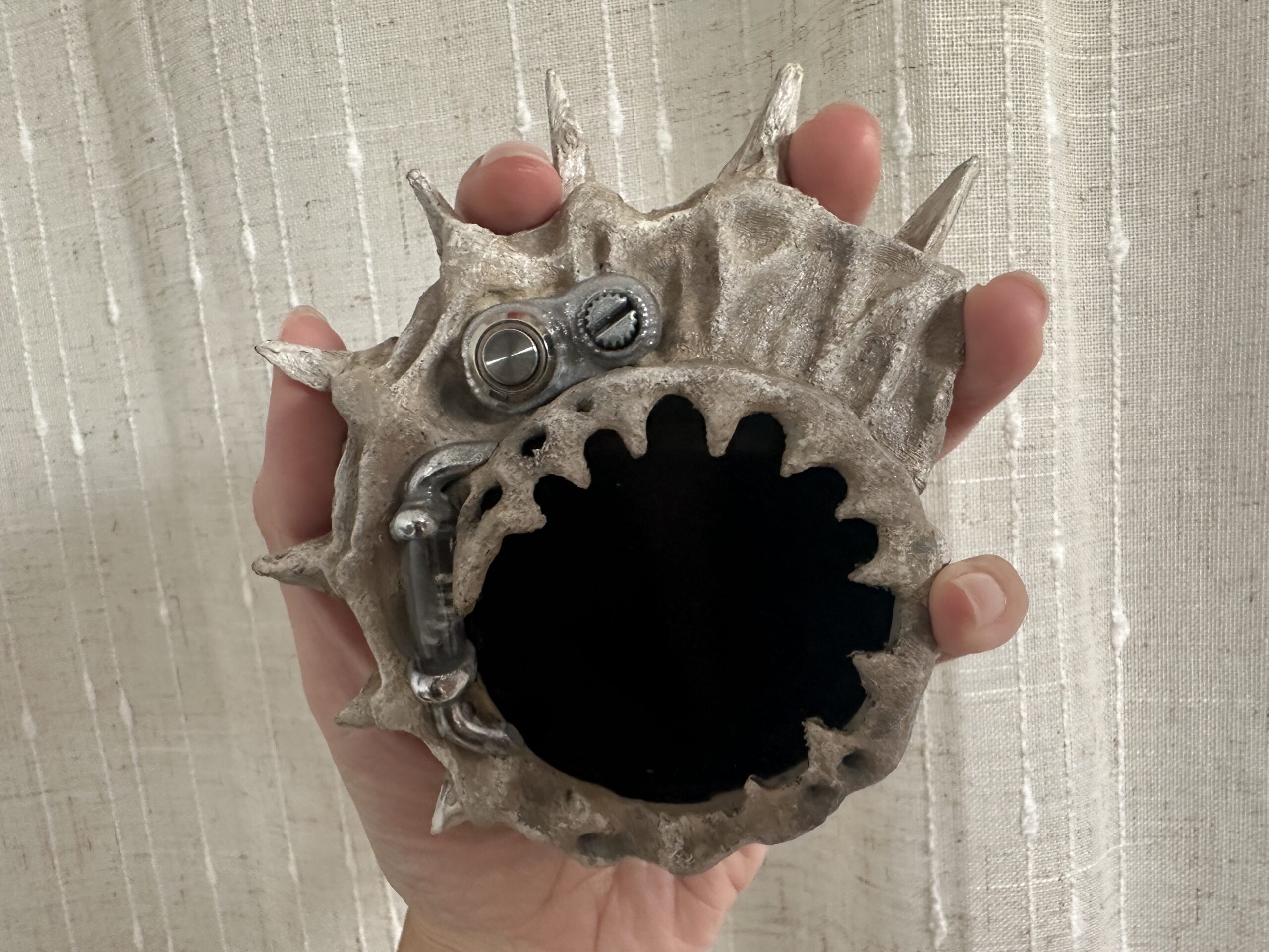 A hand holds a small, spiky gray sculpted shell for a cyberdeck.